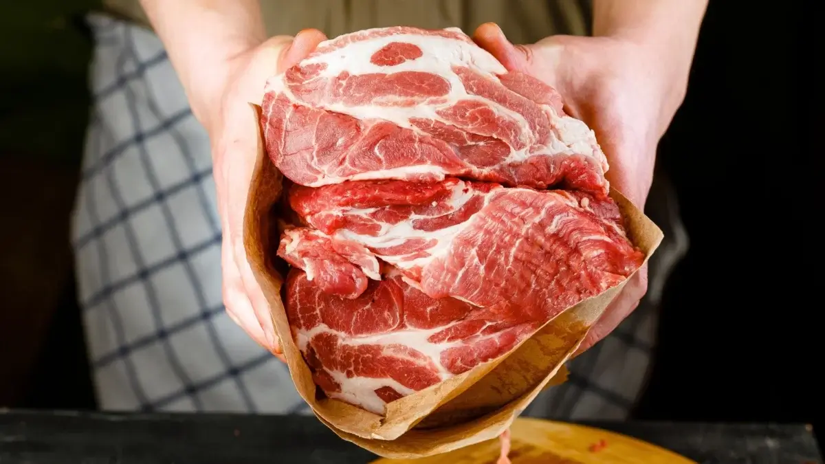 A man holds and displays a bright pink-red, greasy-streaked, sustainable safer meat wrapped in paper.